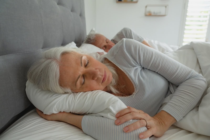 3 Health Benefits for Using Your AC While Sleeping. Senior couple sleeping soundly in their bed.